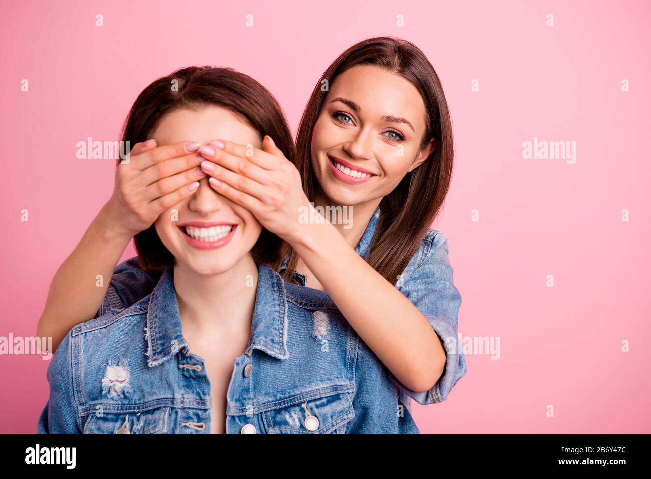 Close up photo two beautiful she her sisters ladies hide eyes hands arms  try guess who unexpected meeting best buddies glad see fellows wear jeans  Stock Photo - Alamy