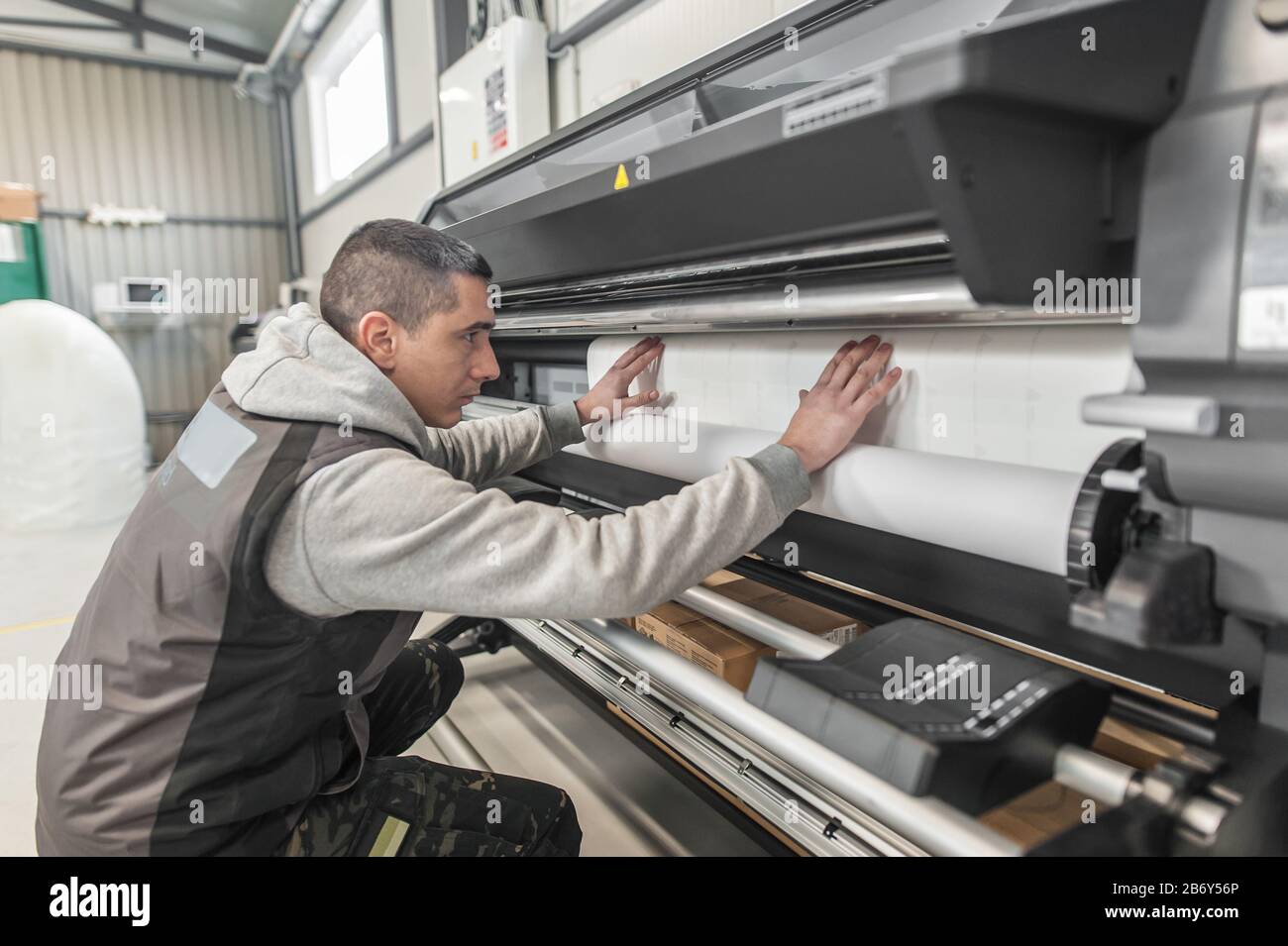 Technician worker operator changes the paper roll on large premium industrial printer and plotter machine in digital printshop office Stock Photo