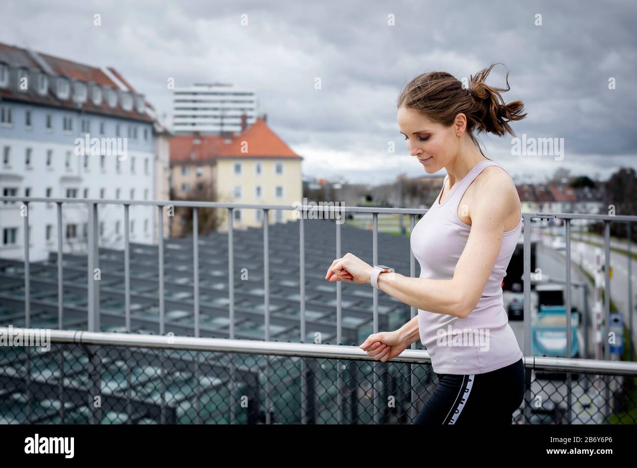 Junge Sportlerin läuft über eine Brücke in der Stadt und überprüft dabei ihre Smartwatch. Young sportswoman runs over a bridge in the city. Stock Photo