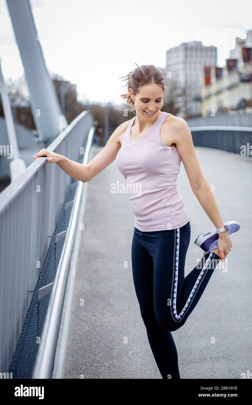 Junge Sportlerin macht Dehnübungen nach dem Sport in der Stadt. Young sportswoman does stretching exercises after sports in the city. Stock Photo