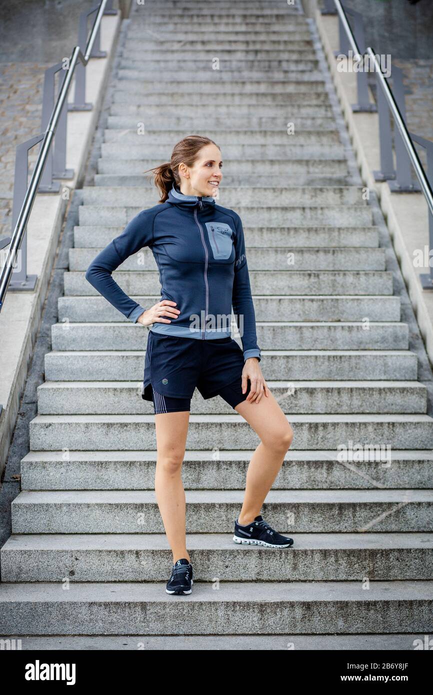 Sporty young women dressed with sportswear stands in front of stairs.  Sportliche junge Frau mit Sportbekleidung steht vor einer Treppe. Stock Photo