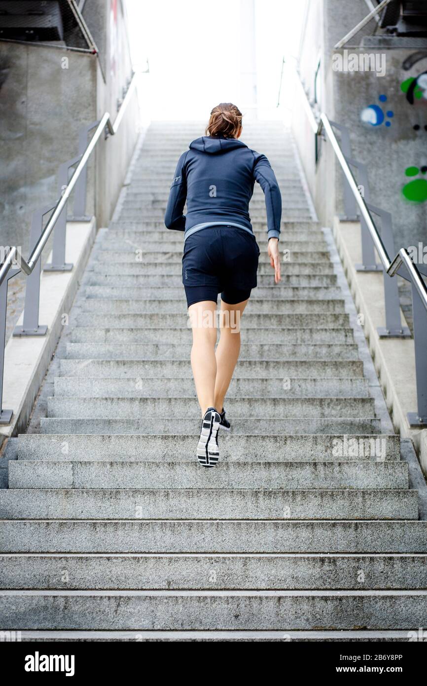 Sporty young women in sportswear runs up stairs, outdoor in the city. Junge Sportlerin in Sportkleidung rennt eine Treppe hinauf. Sport in der Stadt. Stock Photo