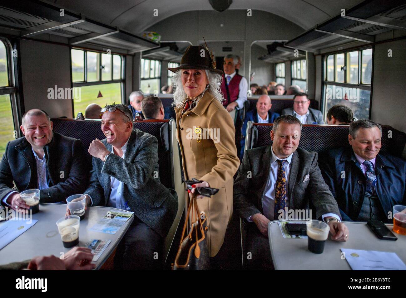 Racegoers move along the aisles aboard a vintage train carriage at Toddington station, Gloucestershire, where people are catching a steam train service to Cheltenham races that is running during the festival. Stock Photo