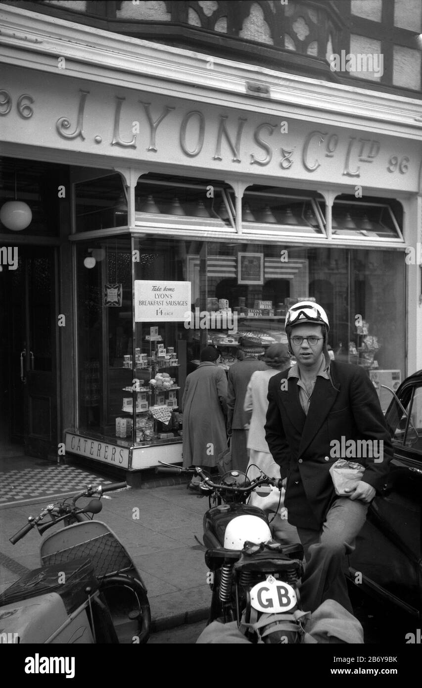 A young man and his motorbike outside a Lyons tearoom in a High Street somewhere in England in the 1950s Stock Photo