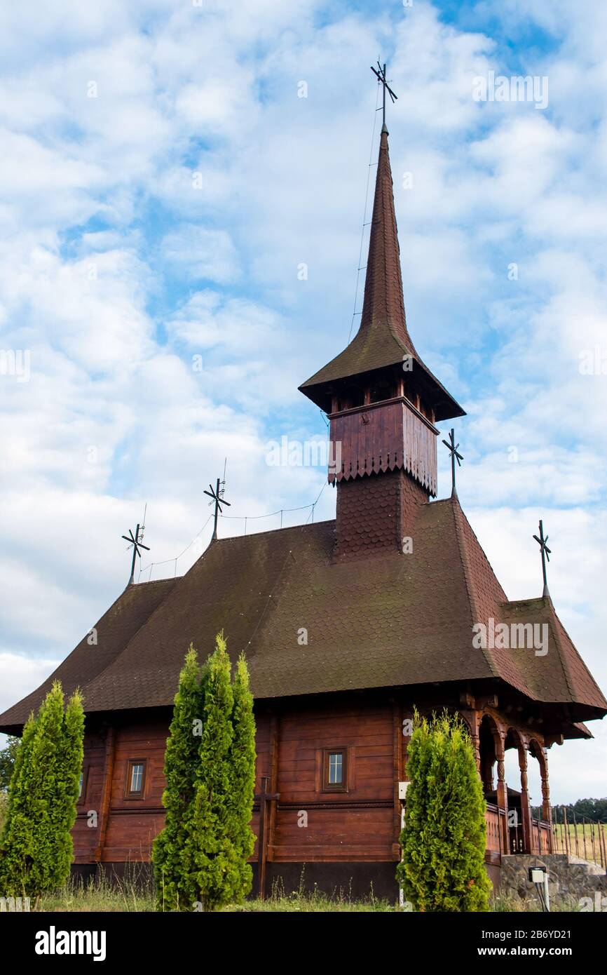 Upwards view of an old wooden church with thuja trees in front on a cloudy sky in Maramures Stock Photo