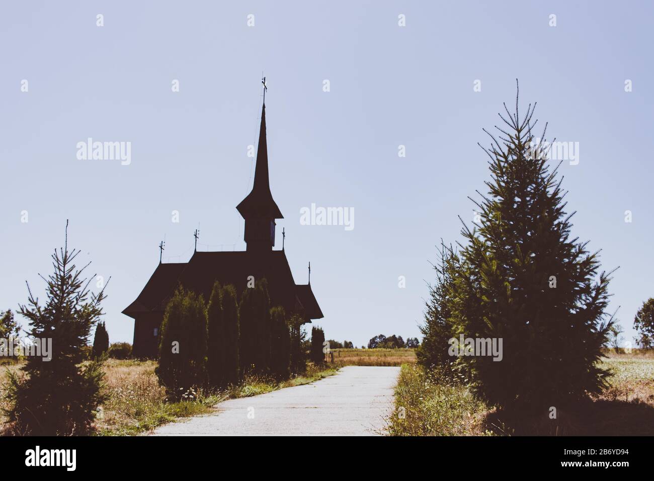 Vintage view of an old wooden church with thuja trees alongside the alleyway in Maramures Stock Photo