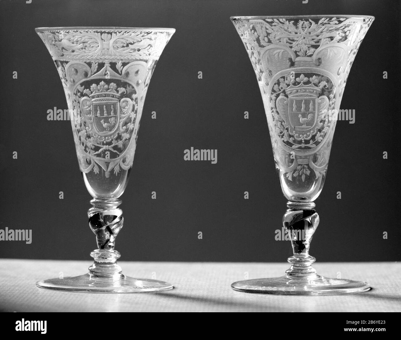 Kelkglas met het wapen van de familie Van Beuningen Chalice Glass of clear, colorless glass. Flat foot. The twisted, baluster stem has a red spiral, an air bubble, and three mereses. The trumpet-shaped cup has a rounded bottom. On the cup, in a cartouche consisting of volutes with matted surfaces with dots and circles, surrounded by sheet of work, there is an oval with the crowned family arms Van Beuningen, flanked by two arms which are bound at the bottom to each other. Along the mouth edge a tire with symmetrical leaf and flower work branches and two pigeons between a serrated edge, and a st Stock Photo