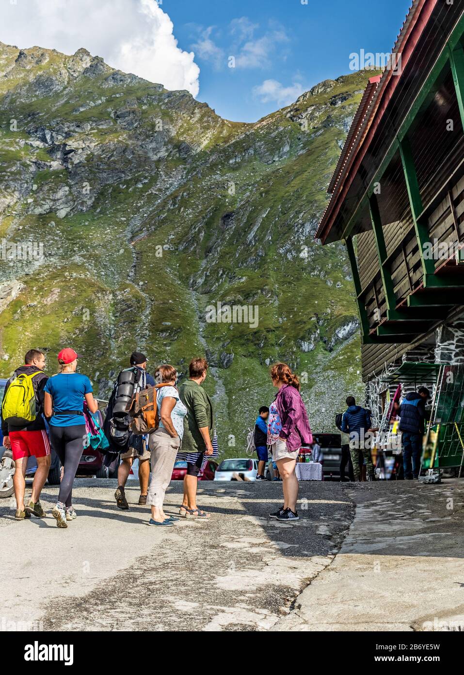 Side View Of A Mountain Chalet With People Walking On A Mountain Road With Mountains In The Background And Puffy Clouds On A Blue Sky Above Stock Photo Alamy