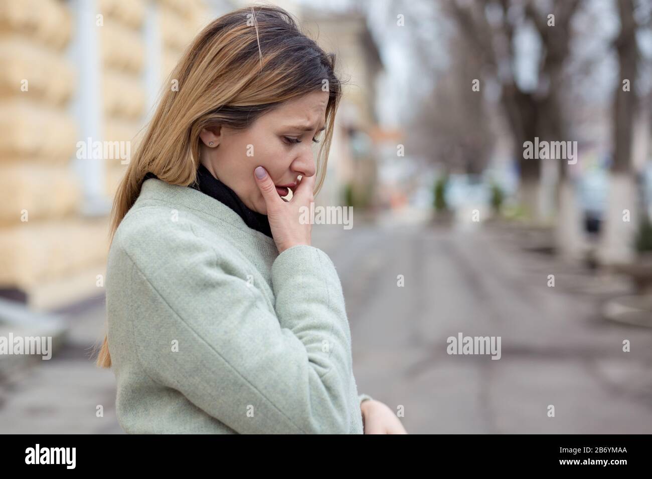 Depressed sad woman in profile almost crying on a city street in Europe, looking down, crying because of her boyfriend betrayal Stock Photo