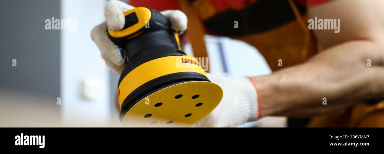 Male construction worker wearing hardhat and protective mask using sanding machine Stock Photo