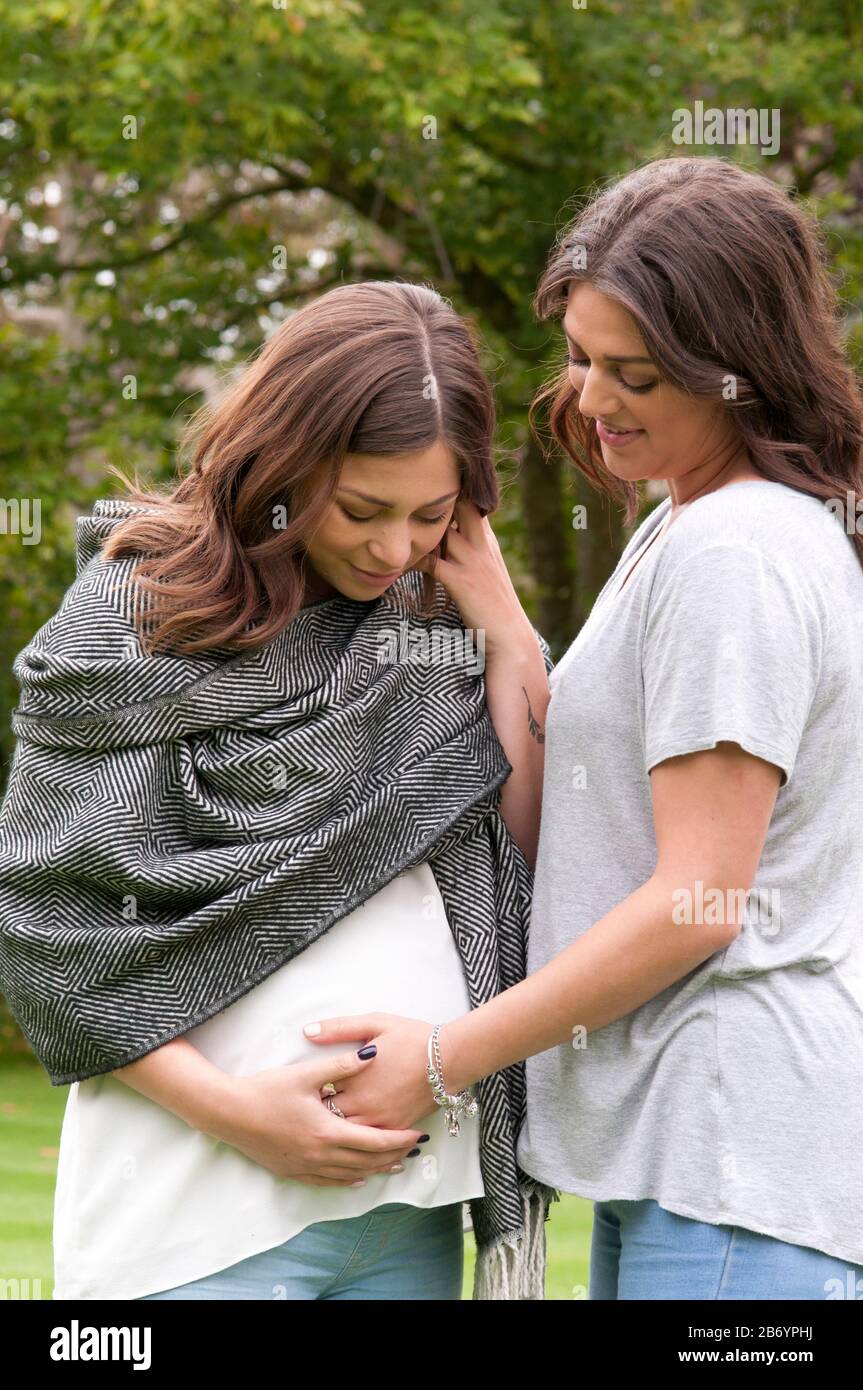 Pregnant young women with her friend feeling her tummy, both smiling Stock Photo