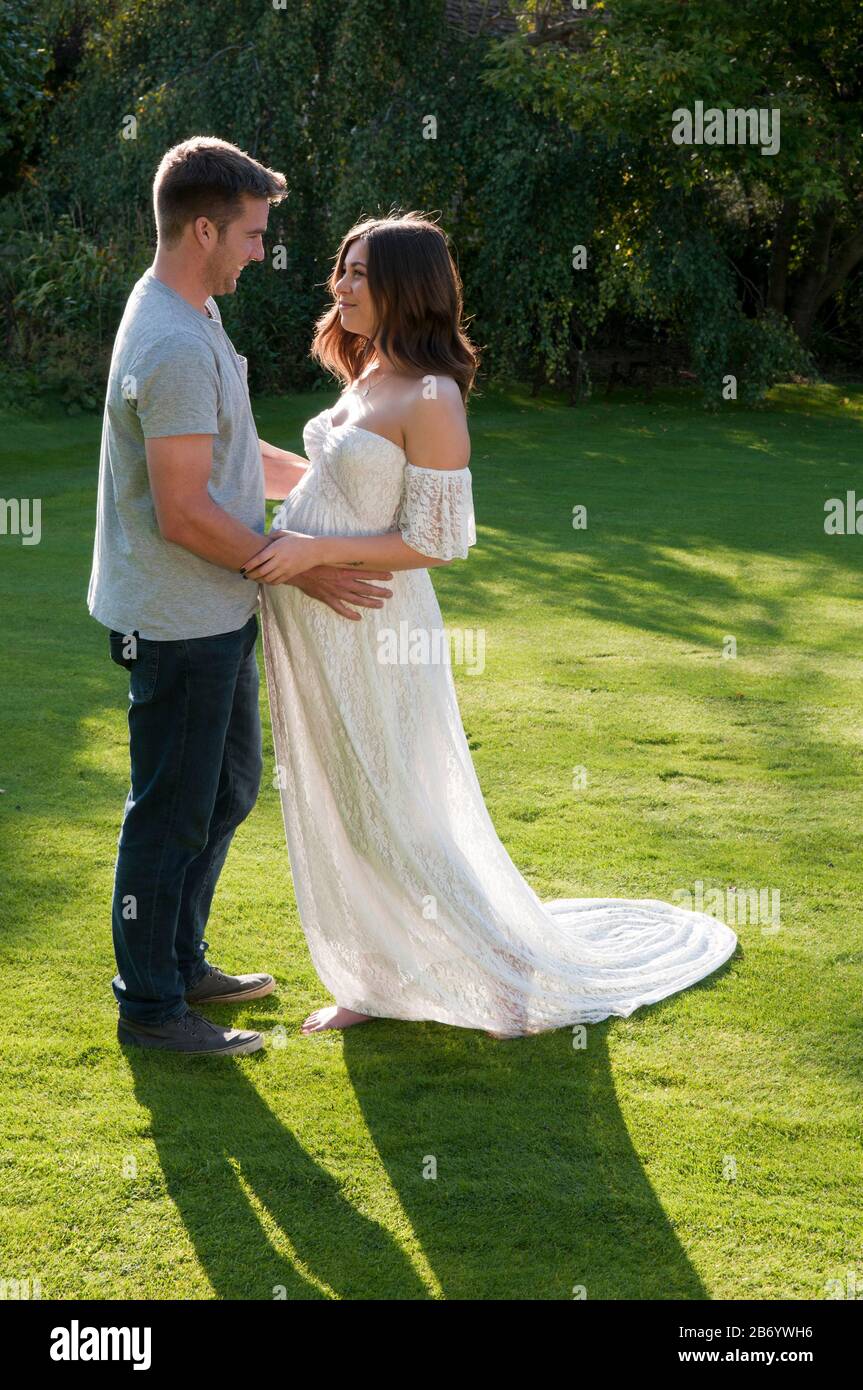 Beautiful pregnant young woman with her partner, standing together with their arms around each other Stock Photo