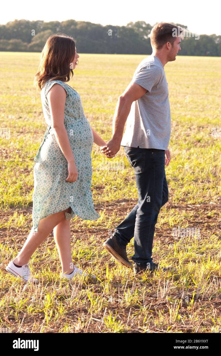 Pregnant young woman walking hand in hand with her partner on a beautiful summers day Stock Photo