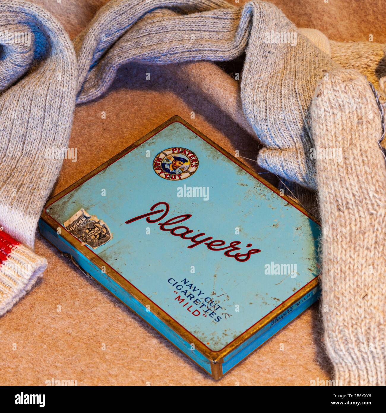 Antique metal tin of Player's Navy Cut cigarettes on a blanket with socks and gloves Stock Photo