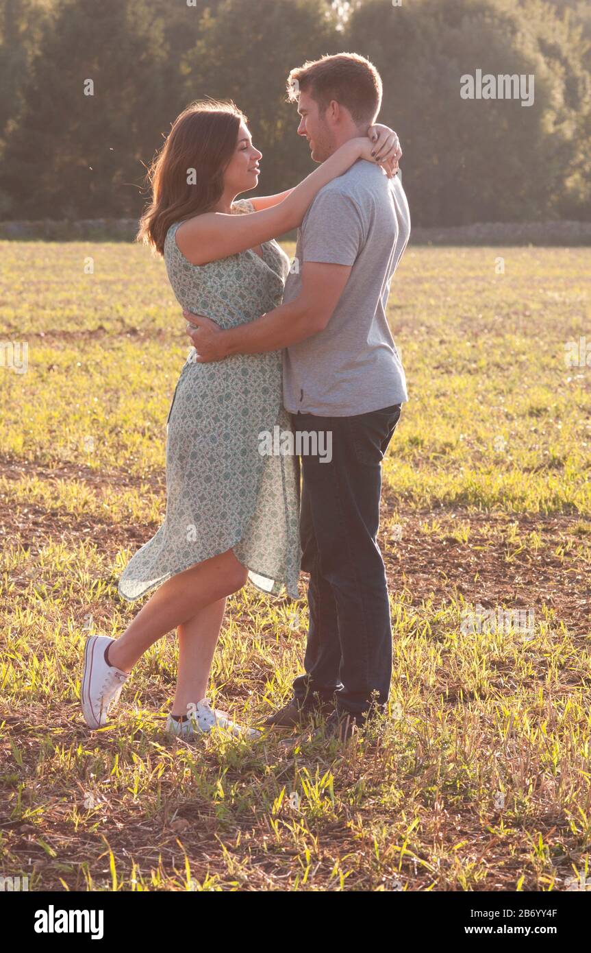 Pregnant young woman with her partner, standing in a field with their arms around each other Stock Photo