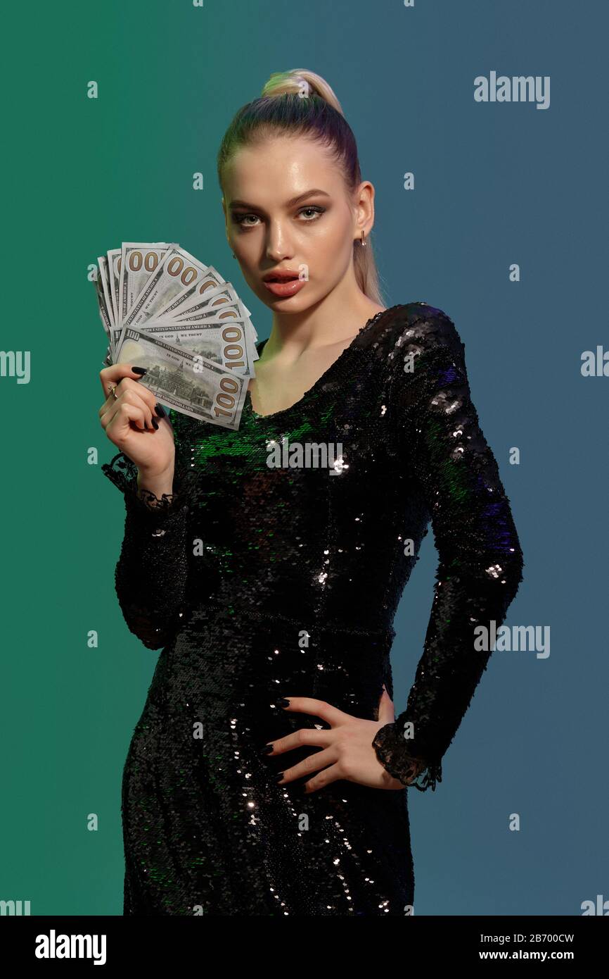 Beautiful blonde girl with ponytail in jewelry and black sequin dress. She is showing some cash hand on hip posing on colorful background. Gambling Stock Photo Alamy