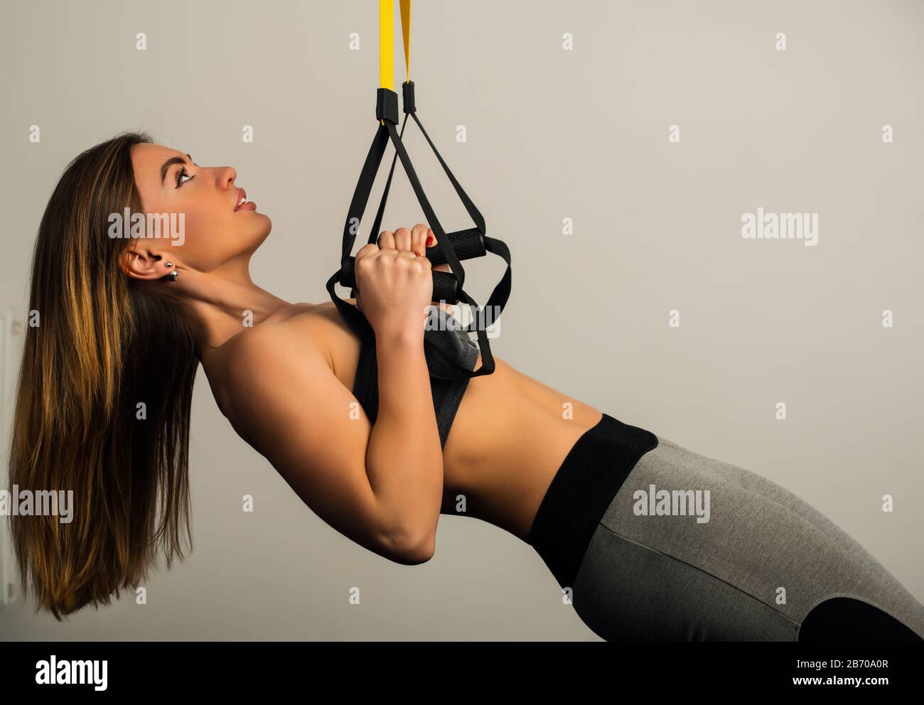 Beautiful young female sportswoman in sportswear holds hands by the handle with sports elastic bands posing on a white background. The concept of spor Stock Photo