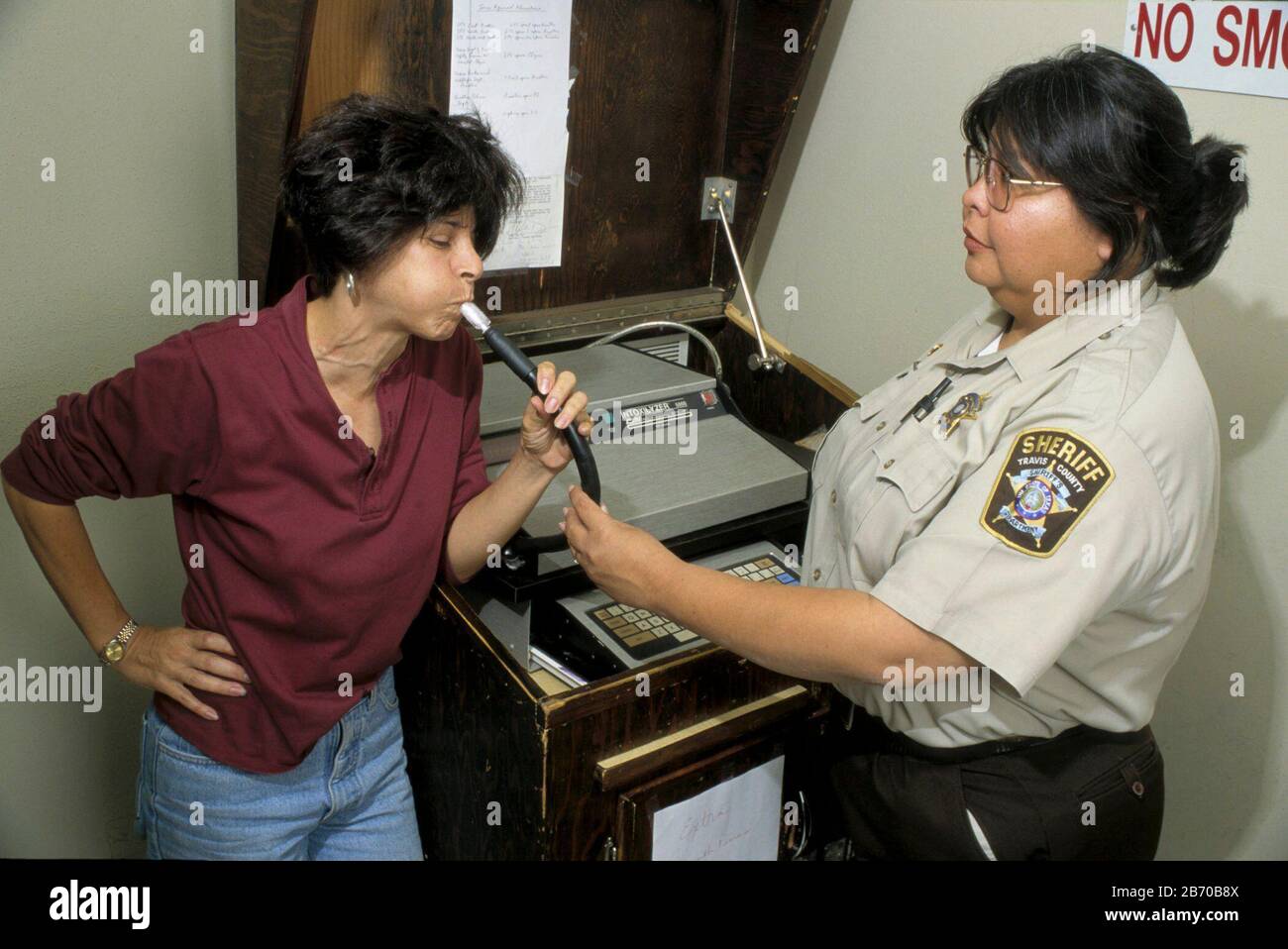 Austin Texas USA, 1997: Driving While Intoxicated (DWI) suspect blows into tube to take breathalyzer test administered by sheriff's office technician. MR ©Bob Daemmrich Stock Photo