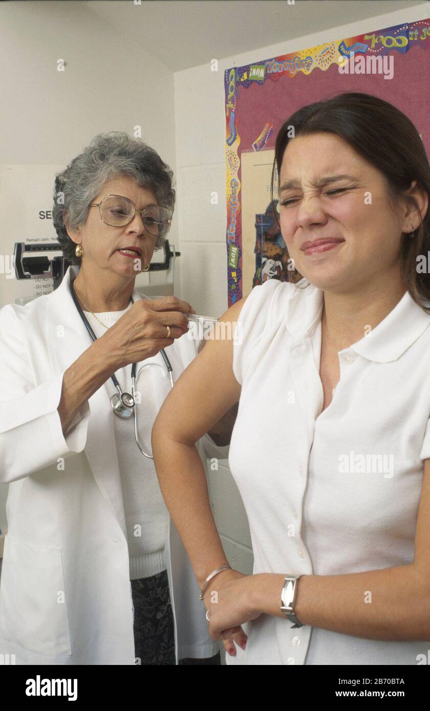 Austin Texas USA: Hispanic teenager is given an immunization shot by Hispanic doctor. MR ©Bob Daemmrich Stock Photo