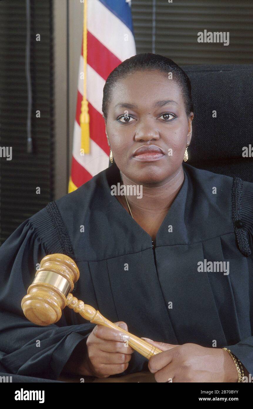 Austin Texas USA, 1997:Female African-American district judge sits at her bench wearing black robe and holding gavel. MR ©Bob Daemmrich Stock Photo