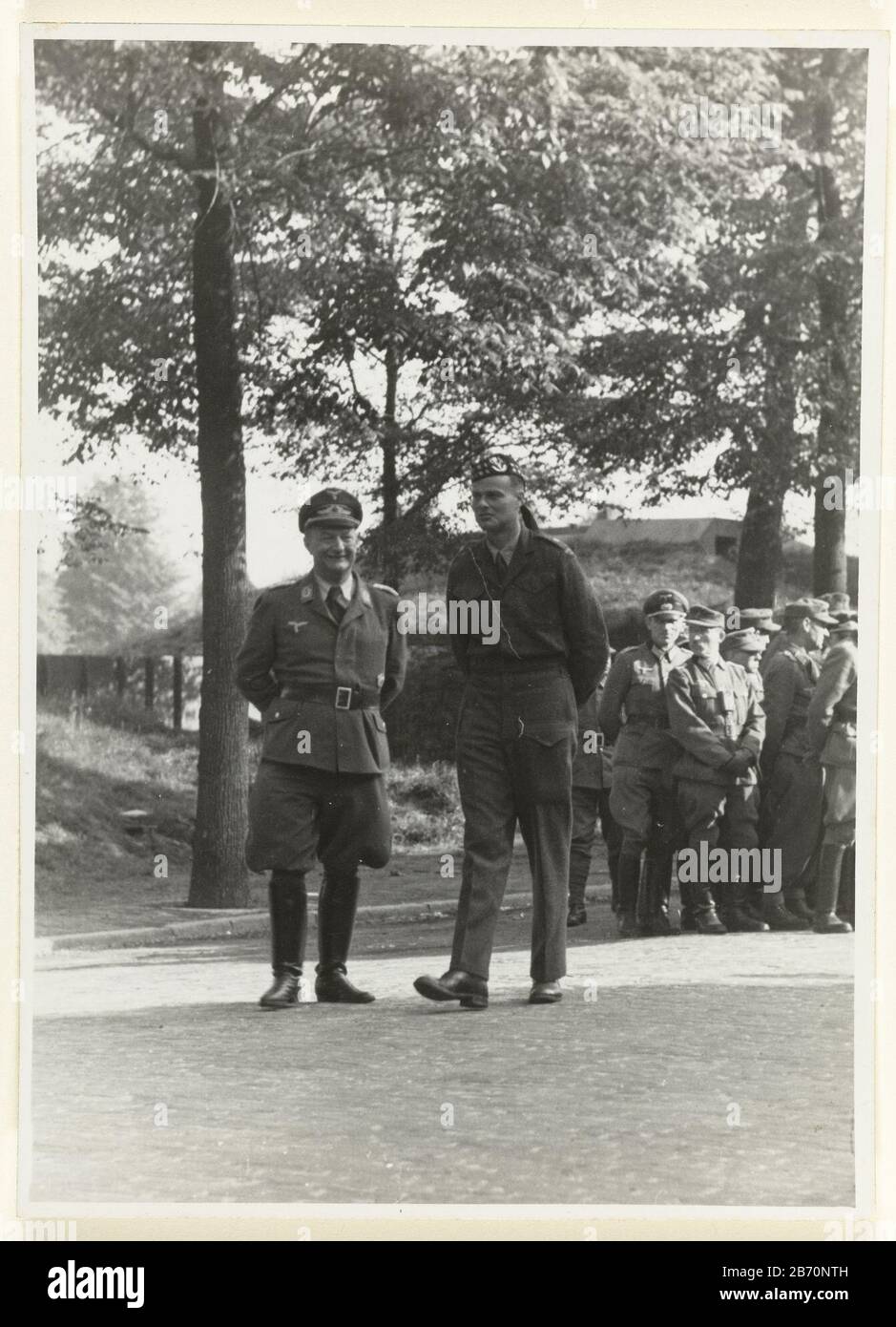Krijgsgevangen Duitsers German prisoner of war guarded by English? military. Left high Luftwaffe officer next to him military of the Allies. In the background krijgsgevangenen. Manufacturer : Photographer: anonymous place manufacture: Netherlands Date: May 1945 Material: paper Technique: Photography Dimensions: H 13 cm. B × 17.5 cm.  Subject: prisoner of war (after the battle) Liberation Second World When: 1945-05 - 1945-05 Stock Photo