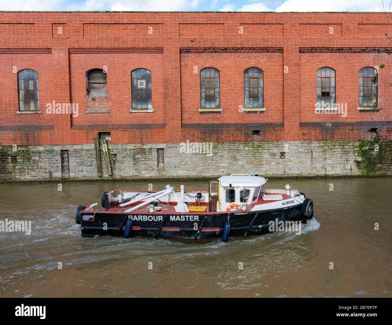 Harbour Master's boat Albion sailing past old brick warehouses on the Feeder Canal of Bristol's Floating Harbour Stock Photo