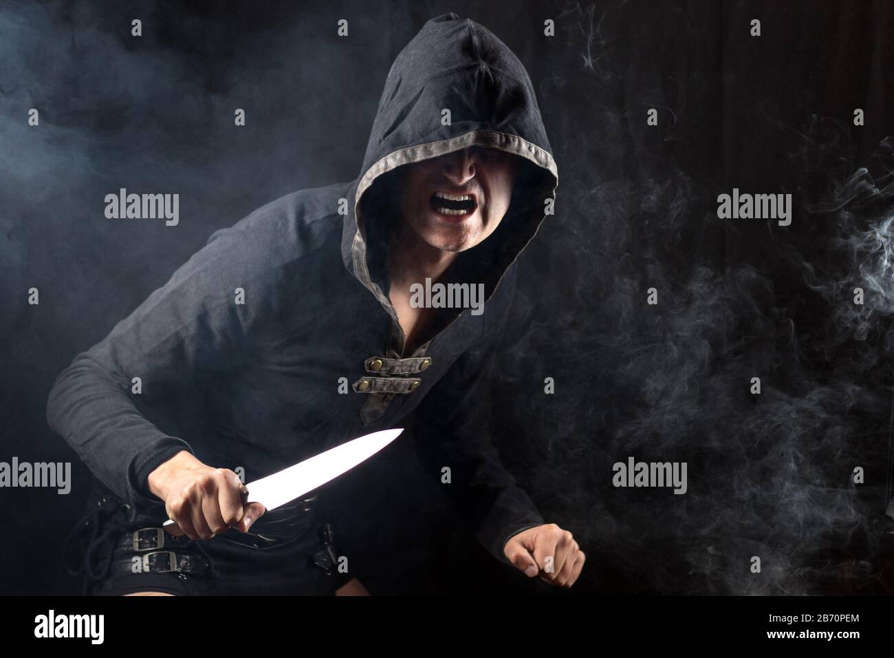 Young man posing in hooded gothic clothes with blade and screaming. Royalty free stock photo. Stock Photo