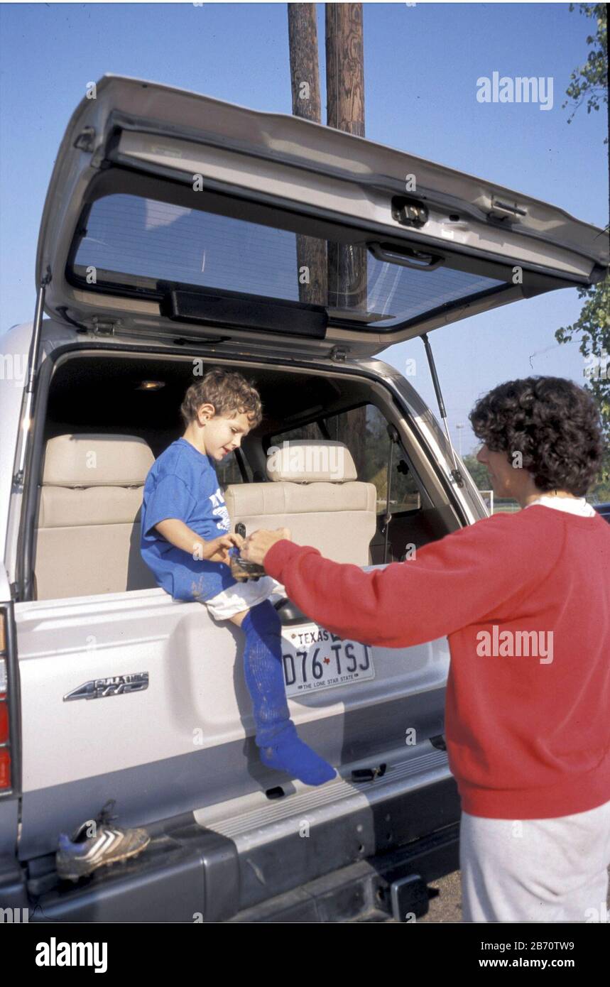Austin, Texas USA, 2001: Mother take muddy shoe from five-year-old son as he sits in back of family vehicle after his recreational league soccer match.  ©Bob Daemmrich Stock Photo