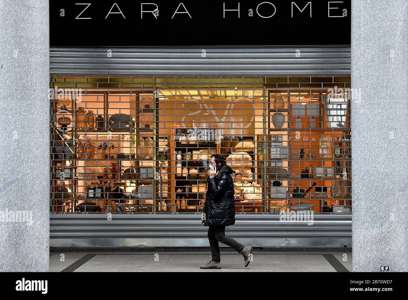 Turin, Italy. 12th Mar, 2020. TURIN, ITALY - March 12, 2020: A man wearing  a respiratory mask walks past a Zara Home shop. The Italian government  shutted down majority of stores to