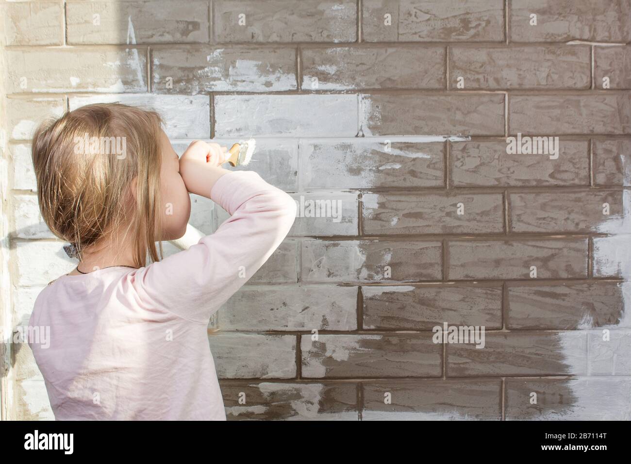 A little girl will paint a brick wall white. Wall painting, repairs in the house. The painter