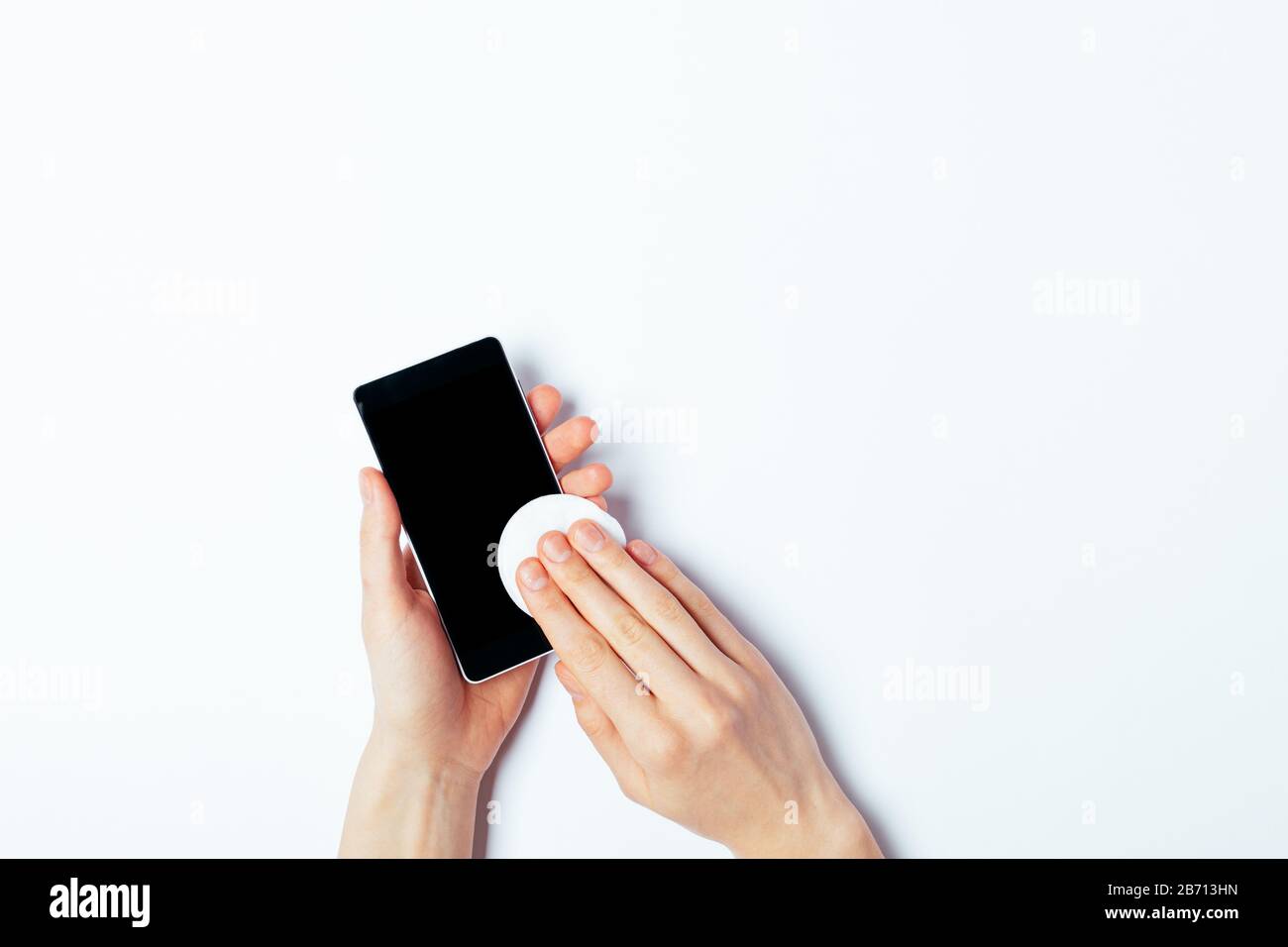 Procedure for disinfecting personal smart phone to protect against viruses, woman's hands wiping surface with cotton pad with alcohol, top view on whi Stock Photo