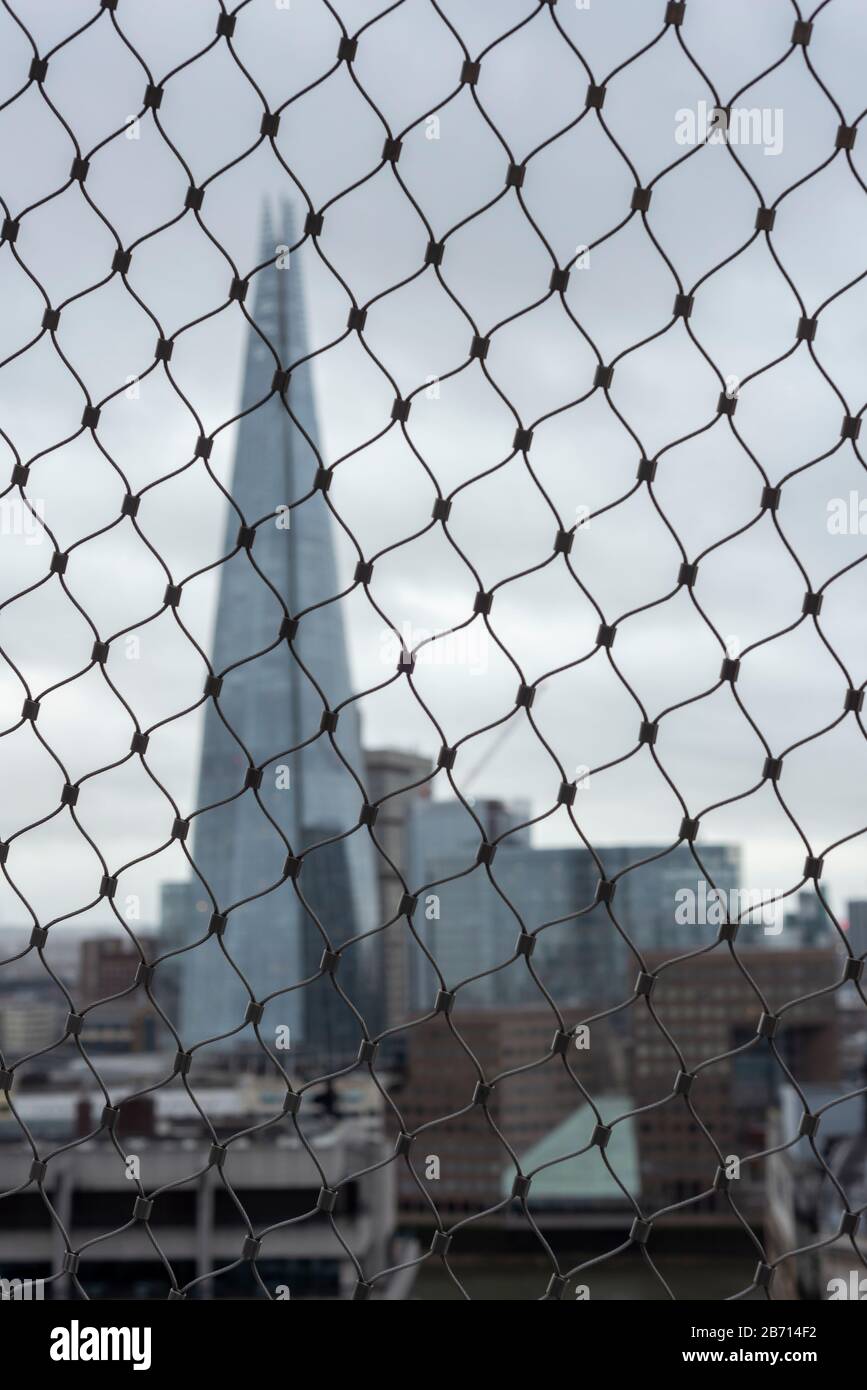 Unusual defocused obstructed view of the Shard building through wire mesh fencing from the top of the Monument on dull cloudy day in London UK Stock Photo