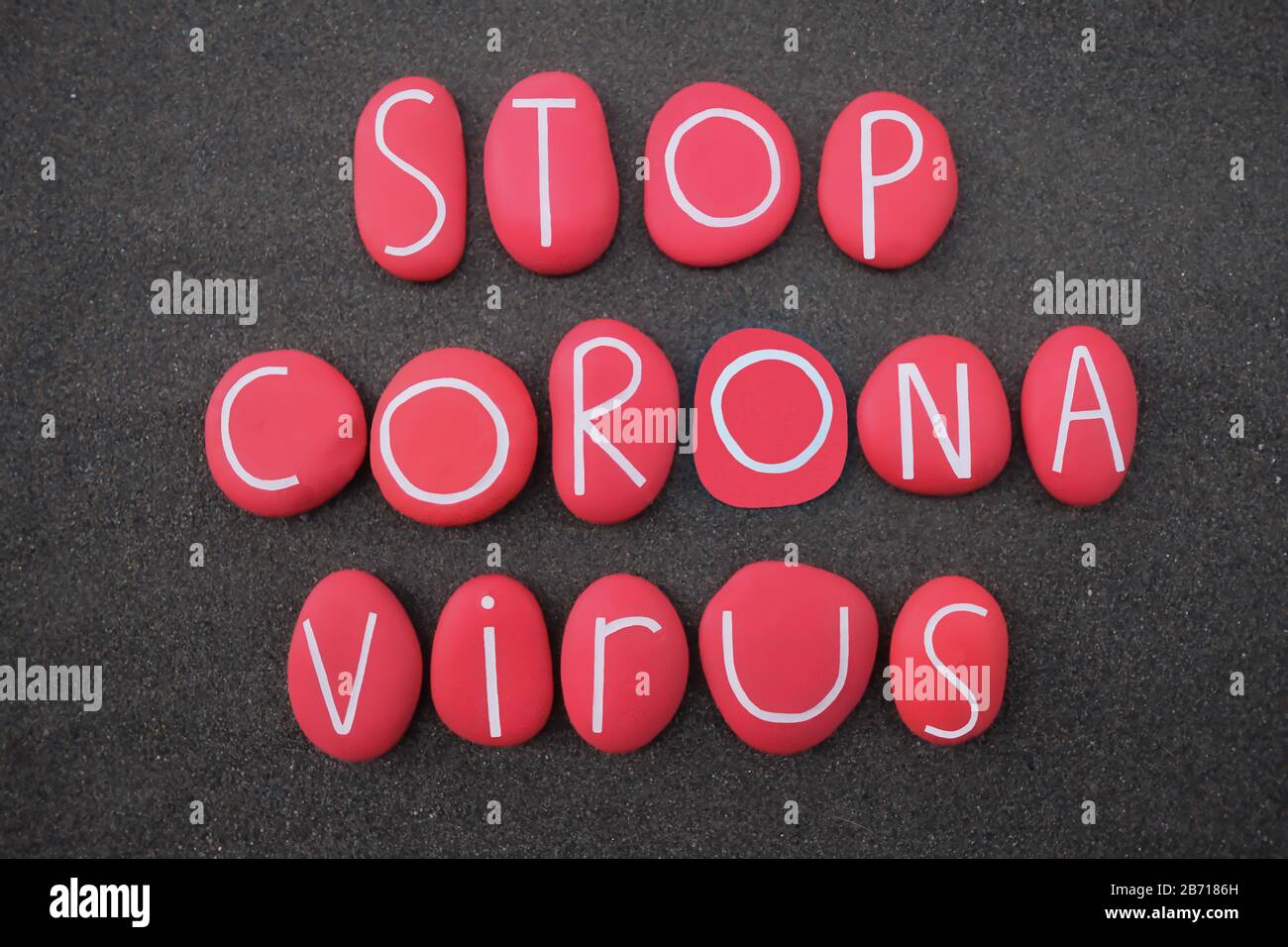 Stop Coronavirus text composed with red colored stone letters over black volcanic sand Stock Photo