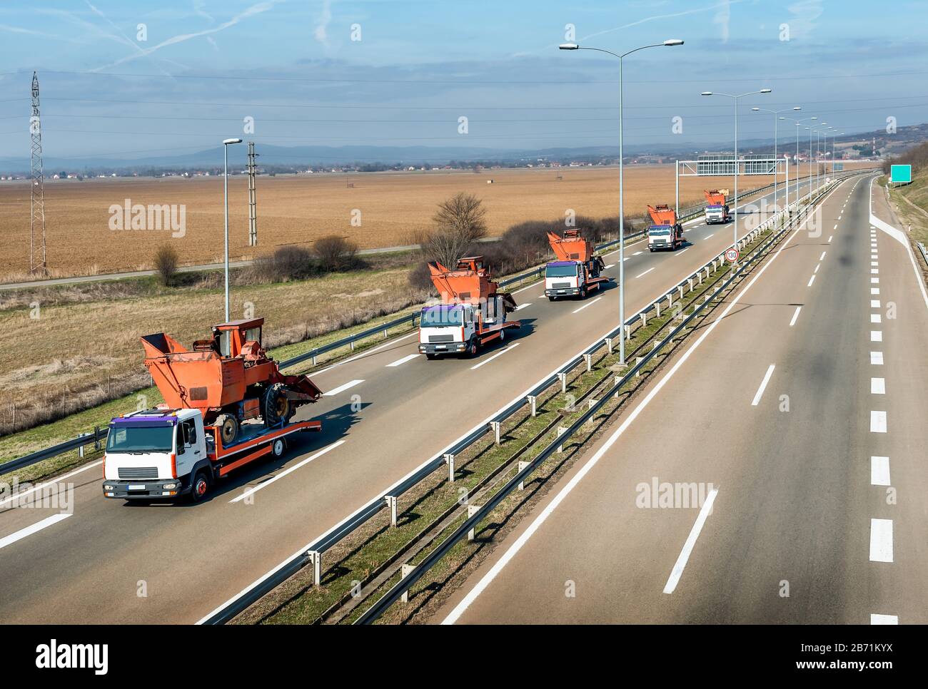 Tow trucks or Flatbed trucks in a convoy towing agricultural or construction machines under a beautiful sky on a highway Stock Photo