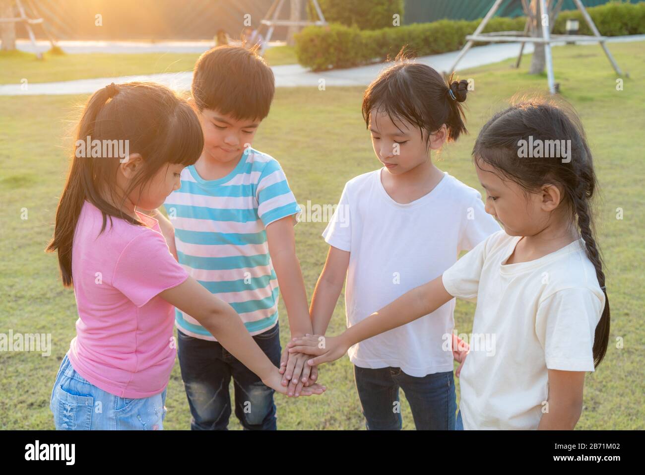 Group of happy young Asian children pile or stack hands togerther outside in city park playground in summer day. Children and recreation concept. Stock Photo