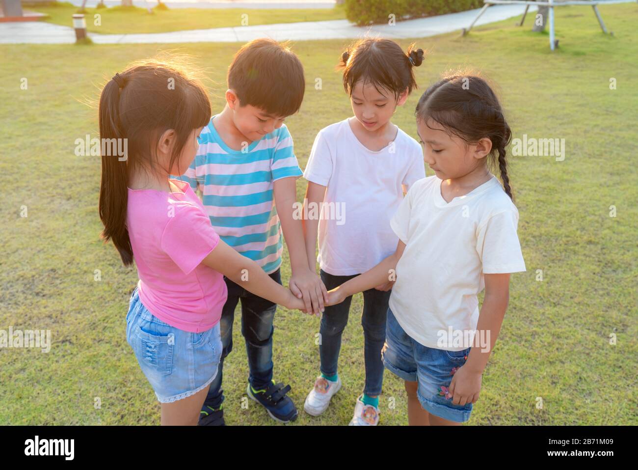 Group of happy young Asian children pile or stack hands togerther outside in city park playground in summer day. Children and recreation concept. Stock Photo