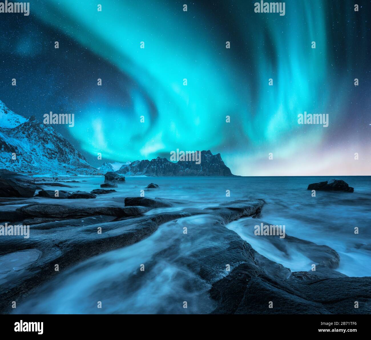 Northern lights over snowy mountain and sandy beach with stones Stock Photo