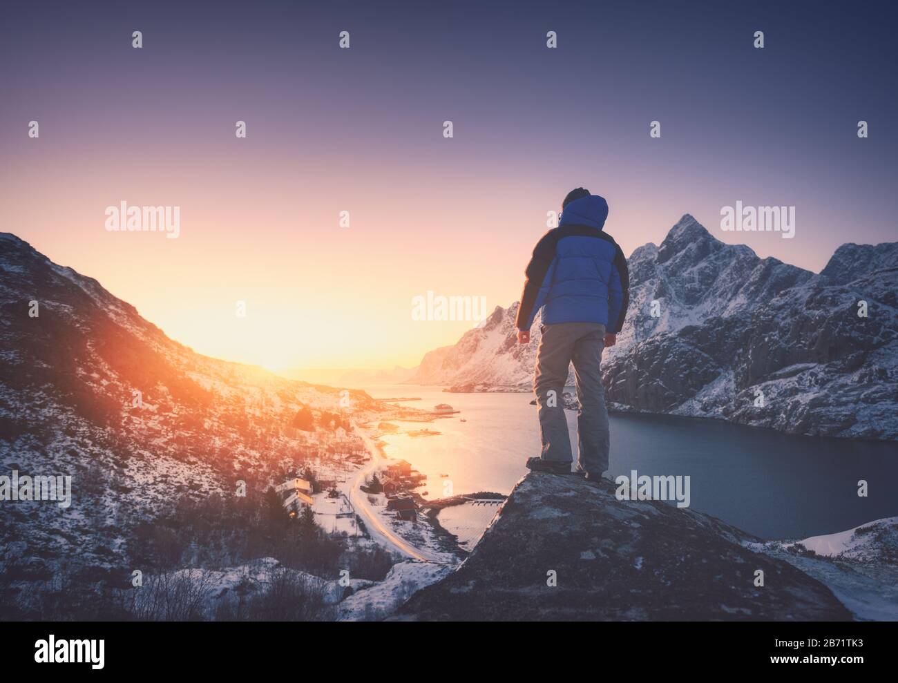 Man is standing on the mountain peak against snowy fjord Stock Photo