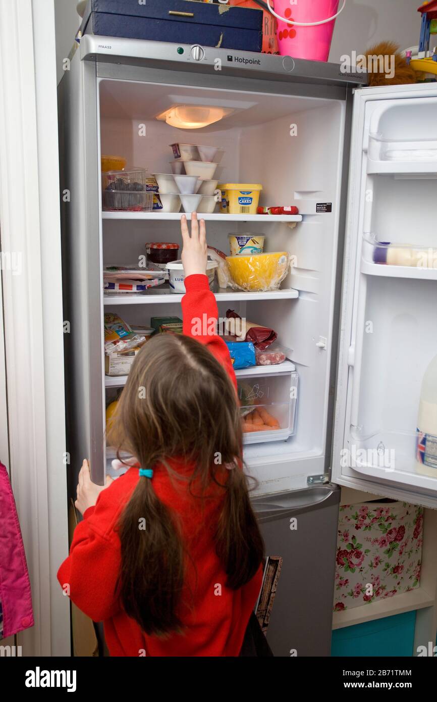 Young girl reaching for food in fridge Stock Photo