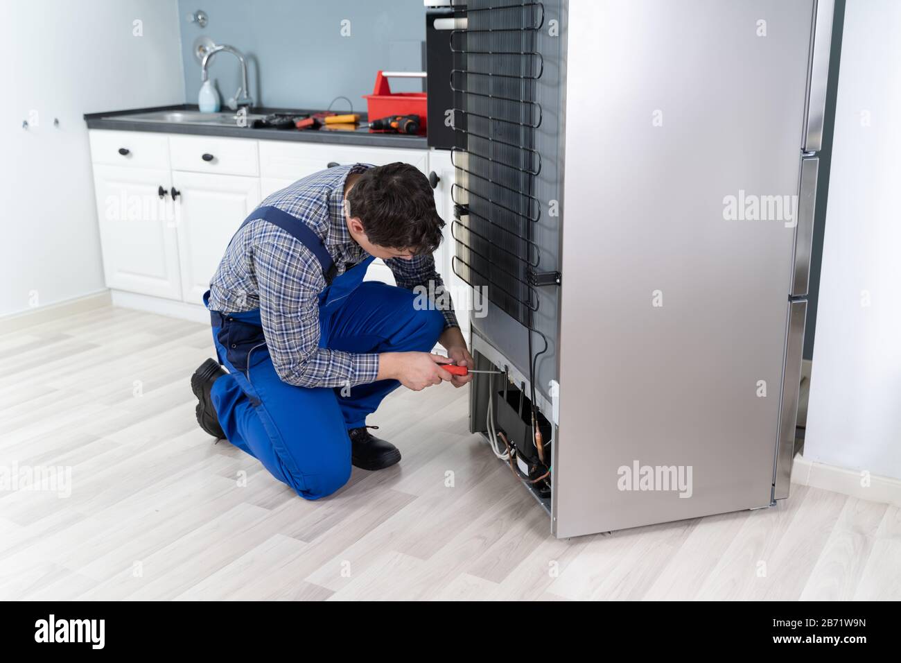 Male Worker Repairing Refrigerator With Screwdriver In House Stock Photo
