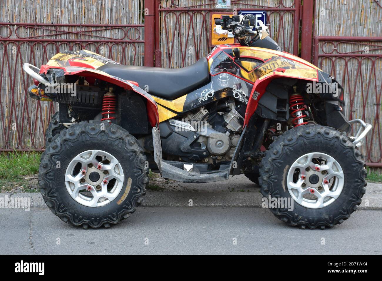 Next to the red metal fence is a quad parked on the sidewalk Stock Photo