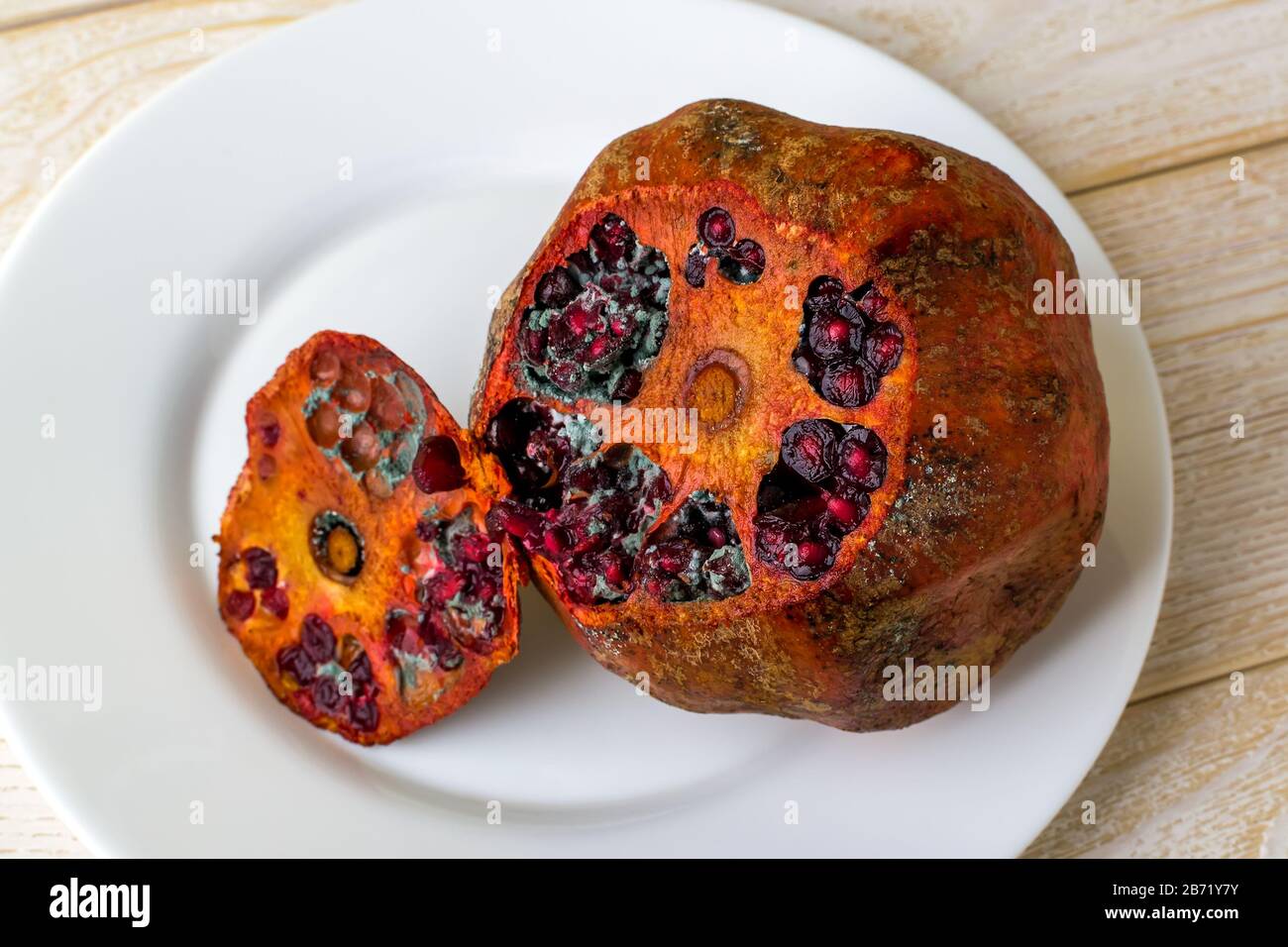 Green fungal mold inside of rotten pomegranate on a white plate. Spoiled fruits and vegetables. Improper or too long food storage. Top view. Stock Photo