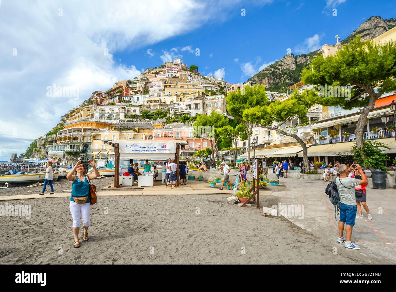 Tourists walk along the boardwalk in front of the sandy beach, cafes and shops at the coastal town of Positano Italy on the Amalfi Coast. Stock Photo