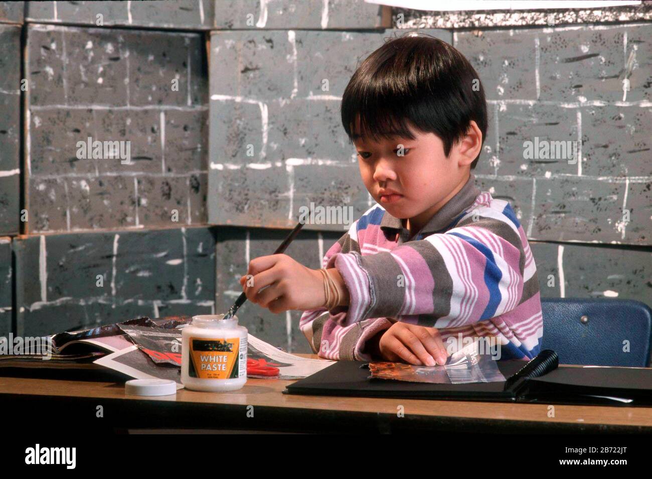 Austin, Texas USA:  Asian-American boy uses glue for pasting pictures in scrapbook for kindergarten project. ©Bob Daemmrich Stock Photo