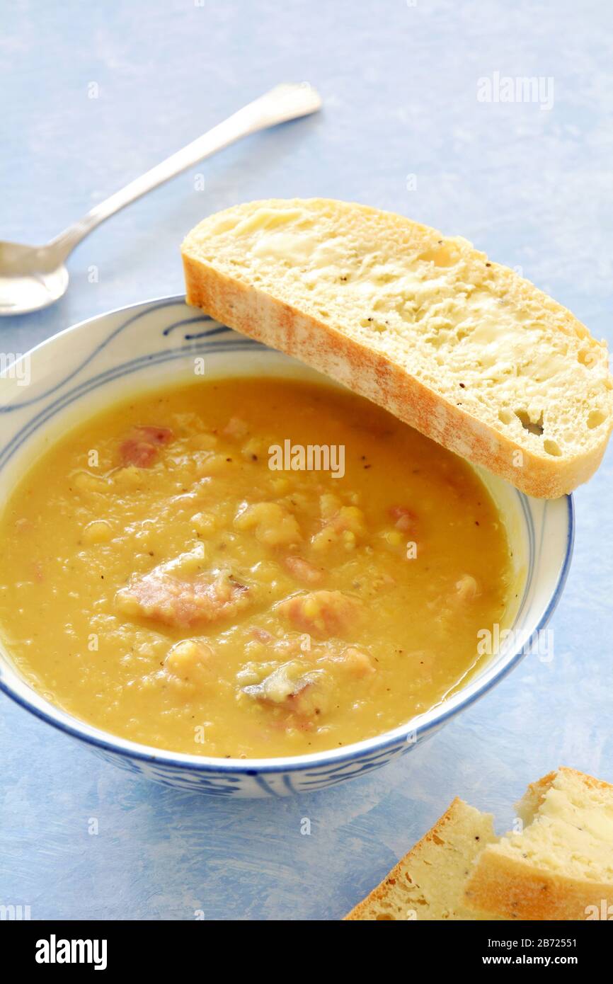 Hearty homemade ham and lentil soup with slice of buttered onion seed cibatta bread on blue background in vertical format. Stock Photo