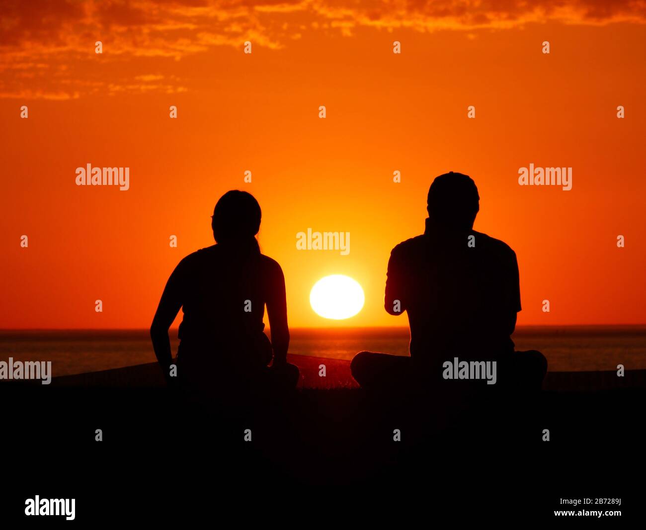 couple silhouettes in front of beautiful orange sunset with clouds Stock Photo