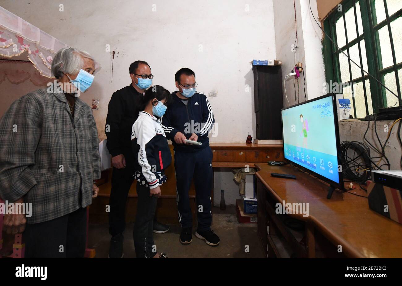 (200313) -- BEIJING, March 13, 2020 (Xinhua) -- Teachers instruct student Huang Yujuan (2nd R) to use online class system on TV at Taiping Town, Wuming District of Nanning City, south China's Guangxi Zhuang Autonomous Region, March 12, 2020. Due to the novel coronavirus outbreak, the new semester has been suspended and students have online classes at home. Given the fact that some poverty-stricken households cannot afford the facilities for online classes, authorities have installed facilities to help the impoverished students learn via online classes. (Xinhua/Lu Boan) Stock Photo
