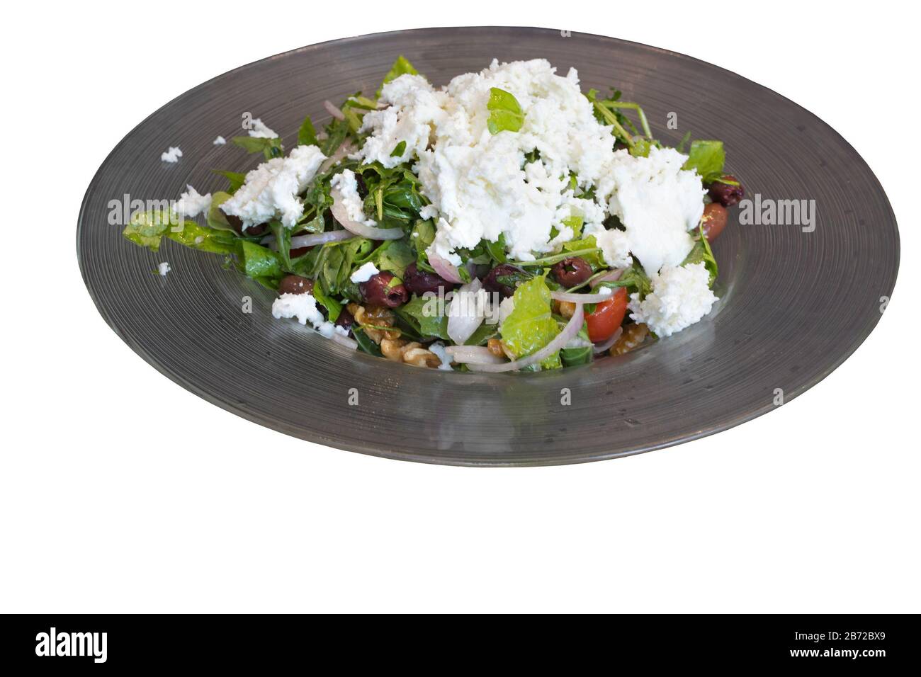 Salad plate with greens, olives, onions, walnuts and tomatoes topped with cheese in a restaurant Stock Photo