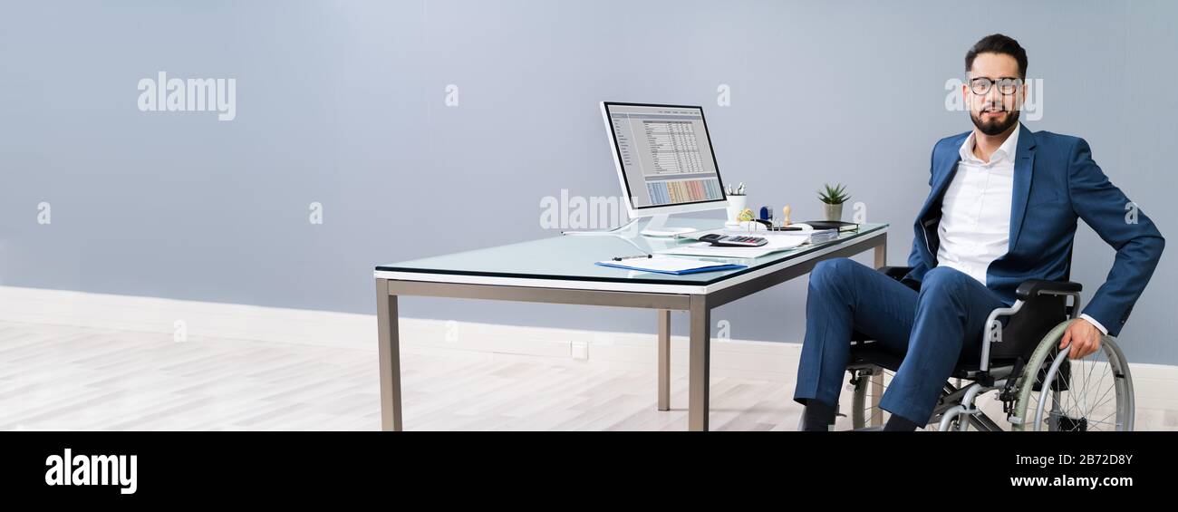 Happy Disabled Businessman On Wheelchair Near Computer Desk In Office