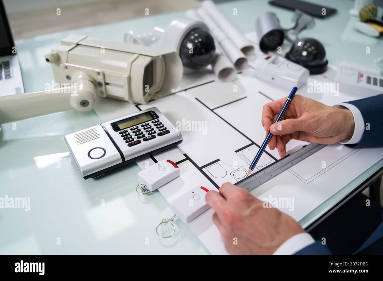 Architect Drawing Blueprint With Various Security Equipment On Desk Stock Photo